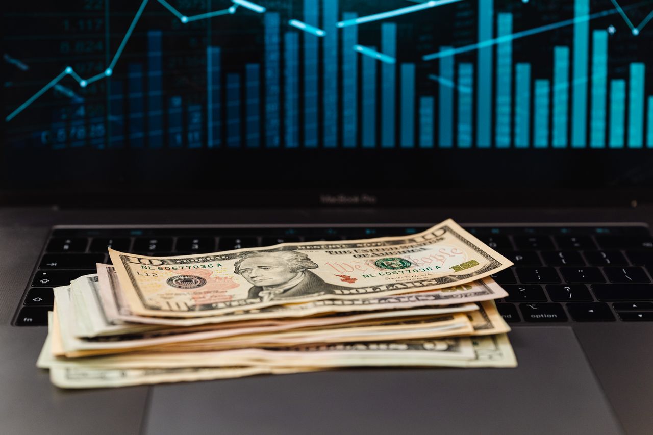 Home US dollar bills on laptop with financial graph in background, symbolizing wealth and technology.